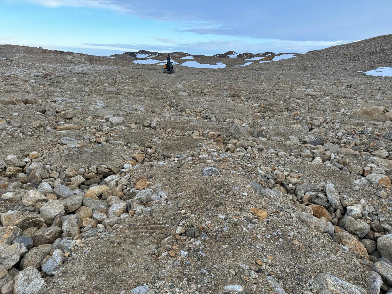 Solo com padrões de pedras numa área plana e sem neve, com o sítio de monitoramento ao fundo.